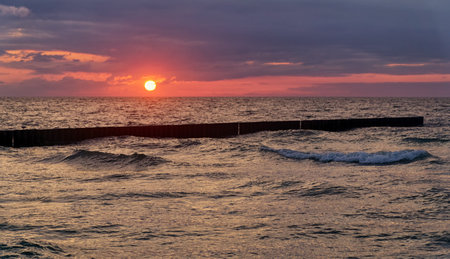 Seascape at sunset in stormy weather. Waves on the sea and dark clouds in the sky. Baltic Sea, Western Pomerania, Poland, Europe.の写真素材