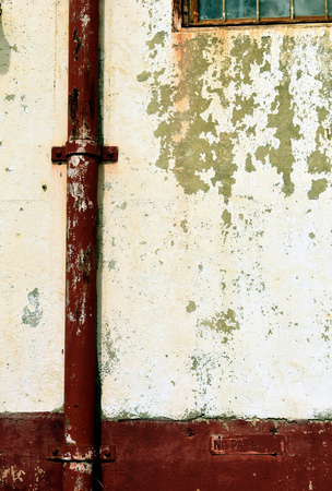 Maroon gutter on white peeling cement wallの写真素材