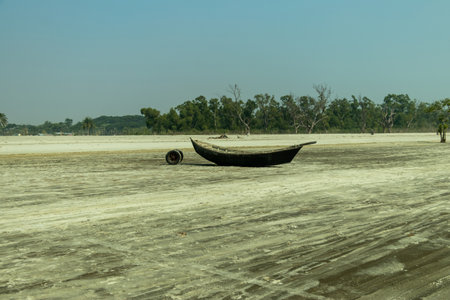 A calm coastline with a flat sandy beach, wooden sampans by the shore, distant greenery, and soft light evoking serenity and authentic coastal or sea beach lifeの写真素材