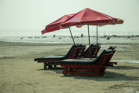 A coastal scene with red and white striped chairs and umbrellas on a wide beach, set against calm...