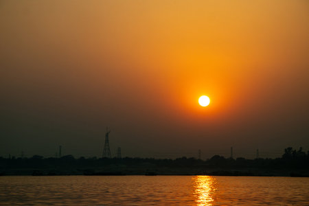A warm, bright light from the brilliant golden sun and its mirrored reflection completely overwhelms the river, sharply with the darkness of the far shoreの写真素材