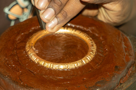 An intricately crafted bangle or bracelet is shown, smooth, cylindrical mandrel made of dark brown polished metal, with ornate gold bands carefully fitted into placeの写真素材