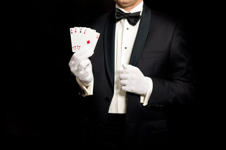 Elegant man in tuxedo holding 4 aces in hand - lucky guy or a magician isolated on black