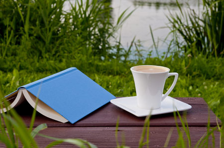 Good place for reading outdoor- garden by the lake. Book and coffee on a park bench.の写真素材