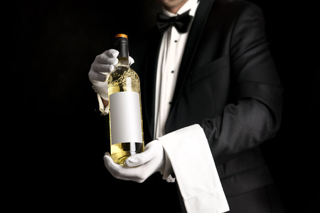 Waiter in tuxedo holding a bottel of white wine with custom etiquetteの写真素材