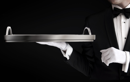 Waiter wearing tuxedo and gloves holding an empty tray isolated on blackの写真素材