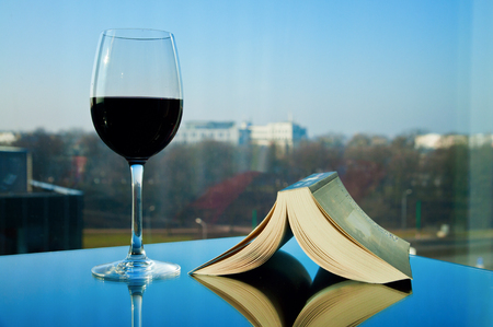 Open book and a glass of red wine over a cityscape. Time for reading.の写真素材