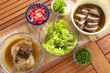 Dinner from the grill: chicken, pork, tomatoes, lettuce, spring onions on wooden table, top viewの写真素材