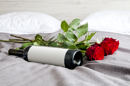 Bottle of wine and red roses on bed - romantic set upの写真素材