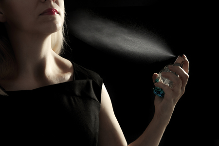 Elegant woman in elegant black dress using parfume isolated on blackの写真素材