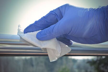 Sanitization of surfaces in public places - hand in disposable glove cleaning a handrailの写真素材