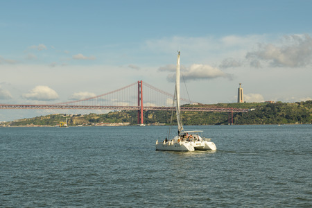 Lisbon, Portugal - April 21, 2018: Small sailboat moving towards the 25th April bridge in Lisbon, Portugal during April 2018のeditorial素材