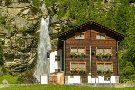 Saas-Balen, Switzerland - August 16, 2019: Wooden house next to beautiful waterfalls in small village of Saas-Balen in canton of Valais, Switzerland during hot sunny day in August 2019のeditorial素材
