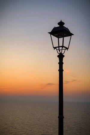 Siluette of old lamp with views on Mediterranean sea during beautiful warm eveningの写真素材