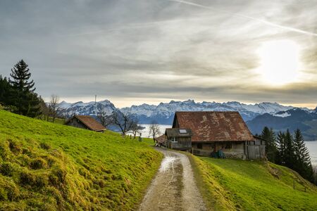 Walking trail leading to small farm with beautiful view on snowy Swiss Alpsの写真素材