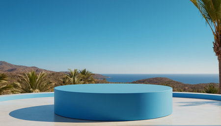 A bright blue cylindrical platform sits on a white surface, casting a shadow. In the background, a vast expanse of blue ocean meets a clear blue sky. Rolling, arid hills dotted with palm trees and other vegetation form the coastline. A palm tree frond is visible in the upper right corner.の素材