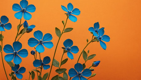 A close-up view showcases several delicate blue flowers with five petals each, set against a solid, warm orange background. The flowers are arranged in a natural, slightly scattered pattern, with visible stems and green leaves. The contrast between the cool blue of the petals and the vibrant orange creates a striking visual. The lighting highlights the textures of the petals and the subtle details of the flower centers.の素材