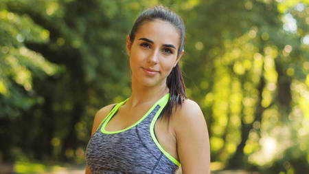 Portrait of cute smiling young woman smiling on camera during the running in the local park.の写真素材