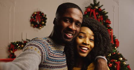 Close up of young happy African American couple videochatting and showing thumb up on a Christmas tree background. Indoor. Portrait. POVの写真素材