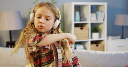 Portrait shot of lovely blonde girl in the big white headphones listening to the music and moving to the rhythm in the nice room at home. Insideの写真素材