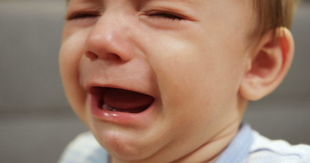 Close up of baby boy face crying. Cute small boy. Blurred background. Portrait. Insideの写真素材