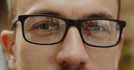 Close up of the male smilid eyes in glasses in glasses loooking to the camera on the blurred background. Outdoor. Portraitの写真素材