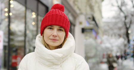 close up of the middle aged beautiful blonde woman in warm winter coat and red hat looking on the...