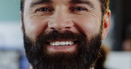 Close up of caucasias man with a beard looking and smiling sincerely straight into the camera. The...
