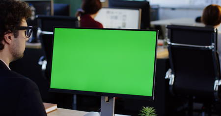 Office worker taping on the PC computer with green screen in the office space. Back view. Chroma key. Indoorの写真素材
