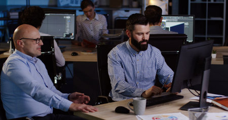 Attractive office worker discussing with his boss startup project while sitting at the computer in...