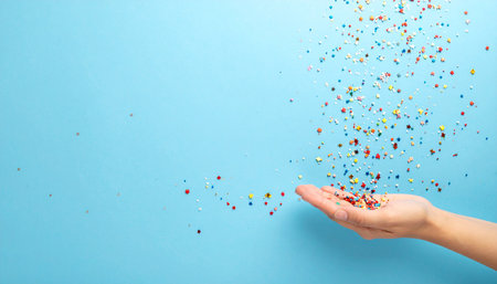 Colorful confetti falling from woman's hand on blue background.の素材
