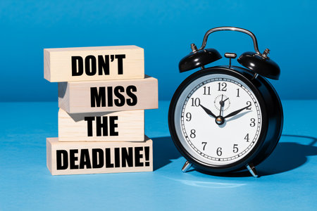 Deadline reminder features a black alarm clock and stacked wooden blocks displaying "Don't Miss The Deadline" against a solid blue backdrop emphasizing the importance of punctuality and time managemeの写真素材