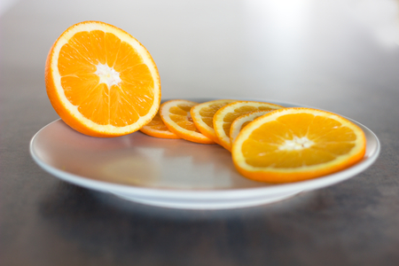 deliciously sweet ripe orange cut into slices served on a plate placed on a light shining bar boardの写真素材