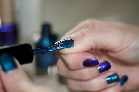 hands of a young woman who is painting her nails with metallized dark green and dark blue nail varnishの写真素材