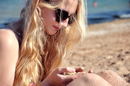 Girl with long hairs on the beach playing with sand and smilingの写真素材
