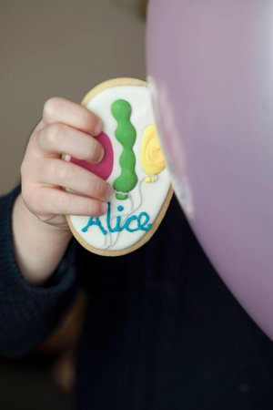 Little Girl Holding Sugar Cookie Decorated with Name and Balloons for Birthday Partyの写真素材