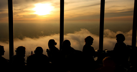 Silhouette of people drinking and having fun. Top floor skyscraper lounge window at sunsetの写真素材