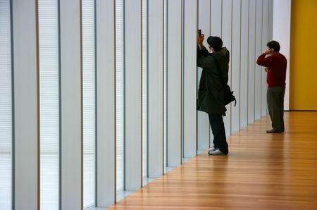 People photographing and talking on the phone in a modern windowed hallwayの写真素材