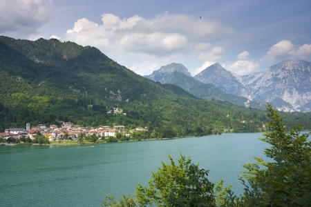 The green waters of Barcis lake, the mountains surrounding it and the village of Barcis itself in Valcellina, Pordenone, Italyの写真素材