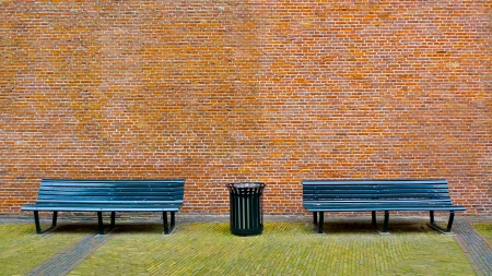 Old black bench and trashcan in front of a red brick wallの写真素材