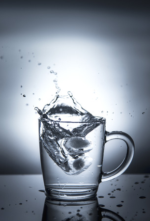 Splash of water in a cup on a grey background.の写真素材