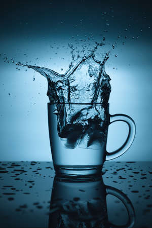 Ice splashing in cup of waterの写真素材