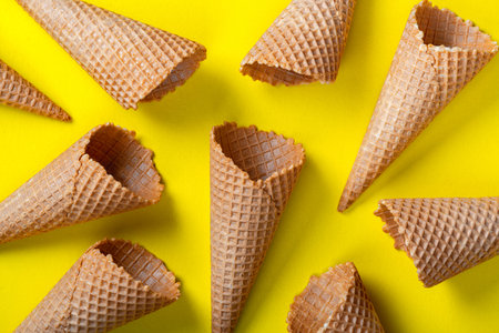Waffle empty ice cream cones on yellow background, flat lay