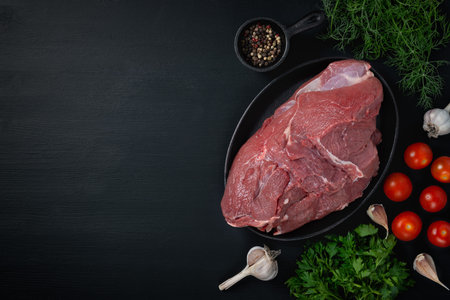 Piece of fresh raw meat, parsley, dill and tomatoes on a black background