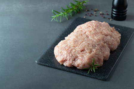 Minced chicken or turkey meat on black board with rosemary and spices.