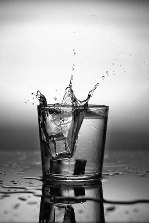 Ice cubes falling into glass of water, close up.の写真素材