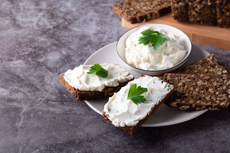 Rye bread on a wooden cutting board with curd cheese and ricotta and herbs.