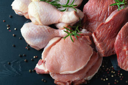 Various types of fresh meat: pork, beef, and chicken on a black tableの写真素材