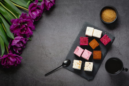 Cakes and coffee on a dark table decorated with a bouquet of beautiful tulips