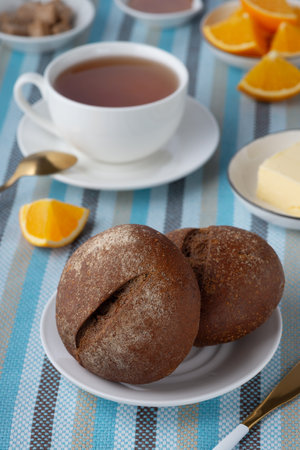 Rye buns and breakfast butter with tea and orange.の写真素材